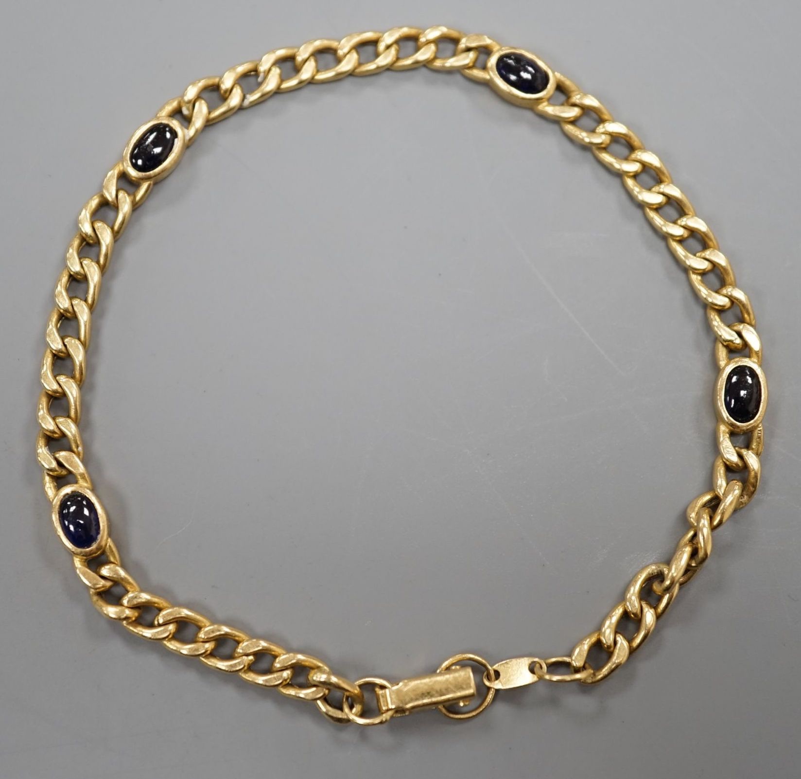 A yellow metal and blue cabochon stone set curb link bracelet, 18cm, gross weight 9 grams.